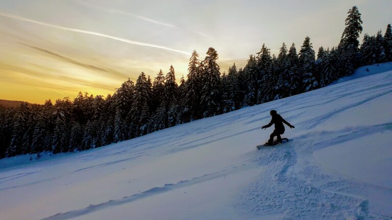 Pulverschneehang im dunkeln, die Sonne geht gerade auf, ein Snowboarder fährt als erstes - Ferienhaus-mit-Bergbahn Baden-Baden