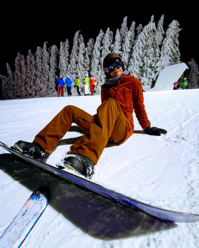 Snowboarderin Nahaufnahme sitzt im Schnee bei Nacht, der Hand ist beleuchtet